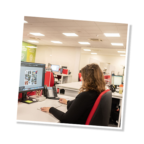 The second image in a slide show, showing a woman at Graphic Services sitting at a computer working on producing an Order of Service