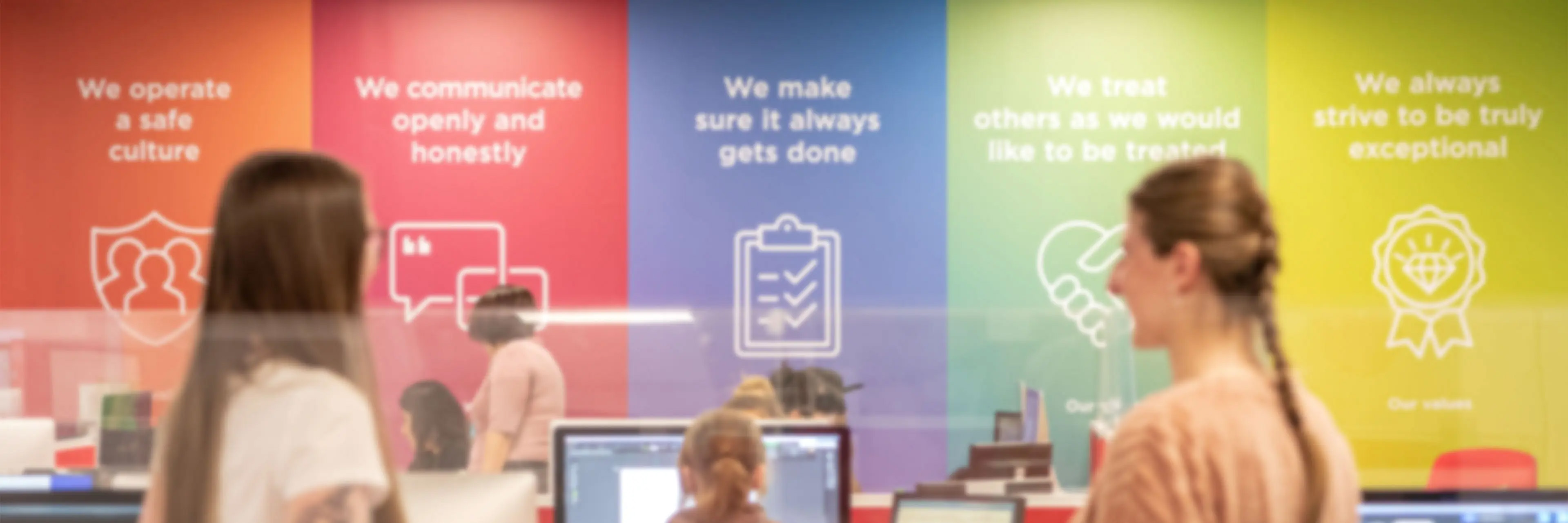 Studio team designing funeral stationery at computers with a colourful company values wall behind them