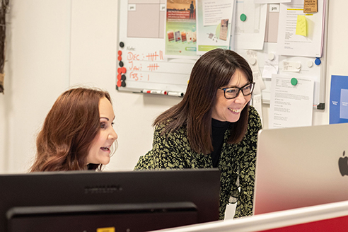 Customer support advisers working together at a computer to help funeral directors with personalised stationery orders
